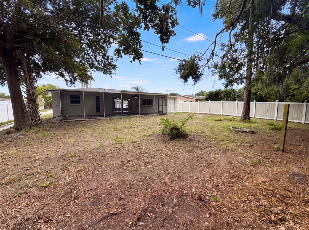 The backyard of a house features a screened-in porch, a large tree, and a white fence — 3400 BAINBRIDGE DRIVE, HOLIDAY, FL