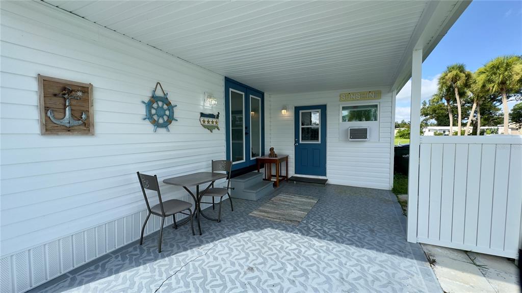 A covered patio features white siding, a small table with two chairs, and blue doors — 6965 APOPO COURT, NORTH PORT, FL