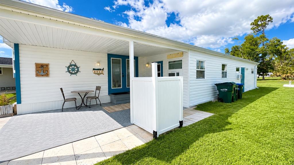 A white mobile home exterior features a covered patio with a table, chairs, and privacy screen — 6965 APOPO COURT, NORTH PORT, FL