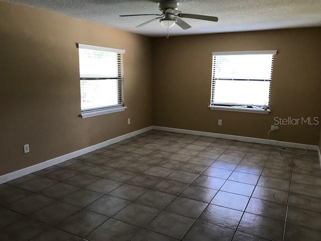An empty room features tan walls, tile flooring, two windows, and a ceiling fan — 437 E OAKWOOD AVENUE, ORANGE CITY, FL