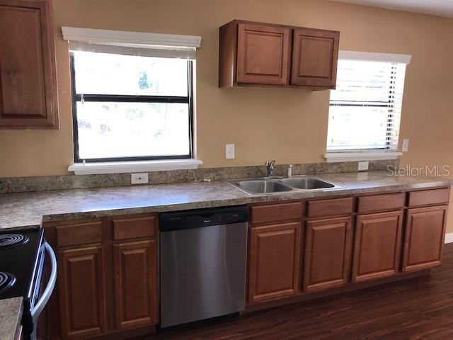 A kitchen features wood cabinets, a stainless steel dishwasher, a double sink, and two windows — 437 E OAKWOOD AVENUE, ORANGE CITY, FL