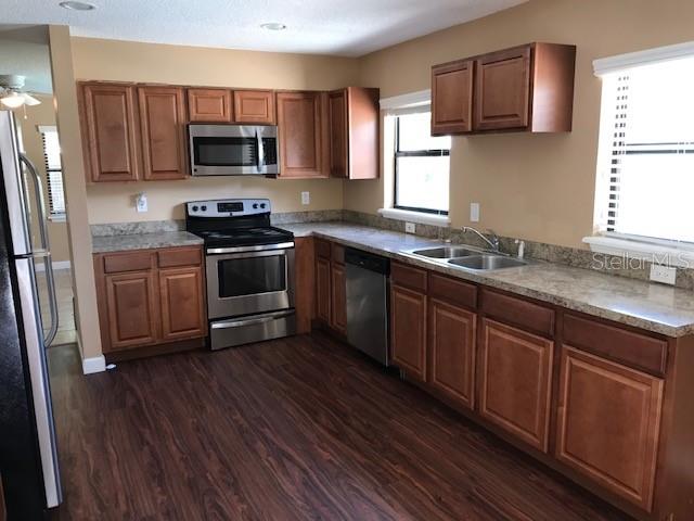 A kitchen features wood cabinets, stainless steel appliances, and laminate countertops over dark wood flooring — 437 E OAKWOOD AVENUE, ORANGE CITY, FL