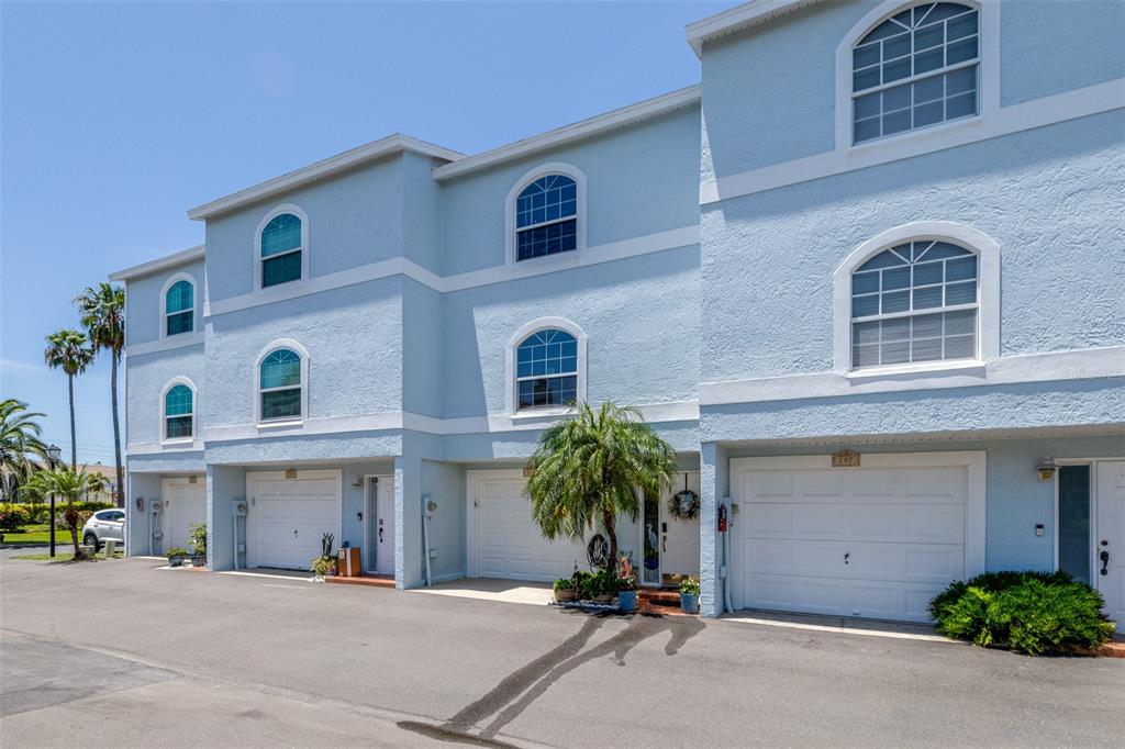 A row of light blue townhouses features white garage doors and arched windows under a clear sky — 751 PINELLAS BAYWAY S UNIT 208, TIERRA VERDE, FL