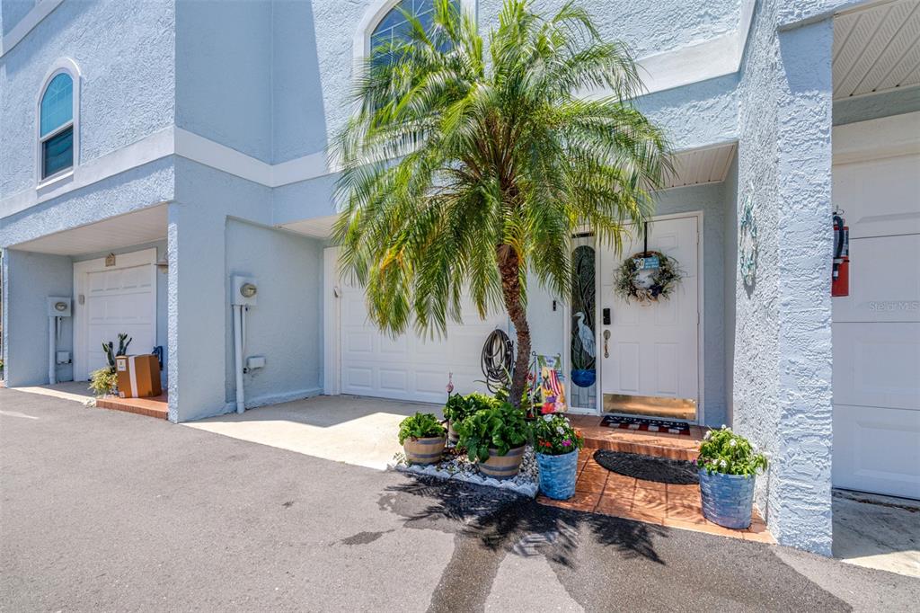 A light blue townhouse exterior features a palm tree, potted plants, and a white door — 751 PINELLAS BAYWAY S UNIT 208, TIERRA VERDE, FL