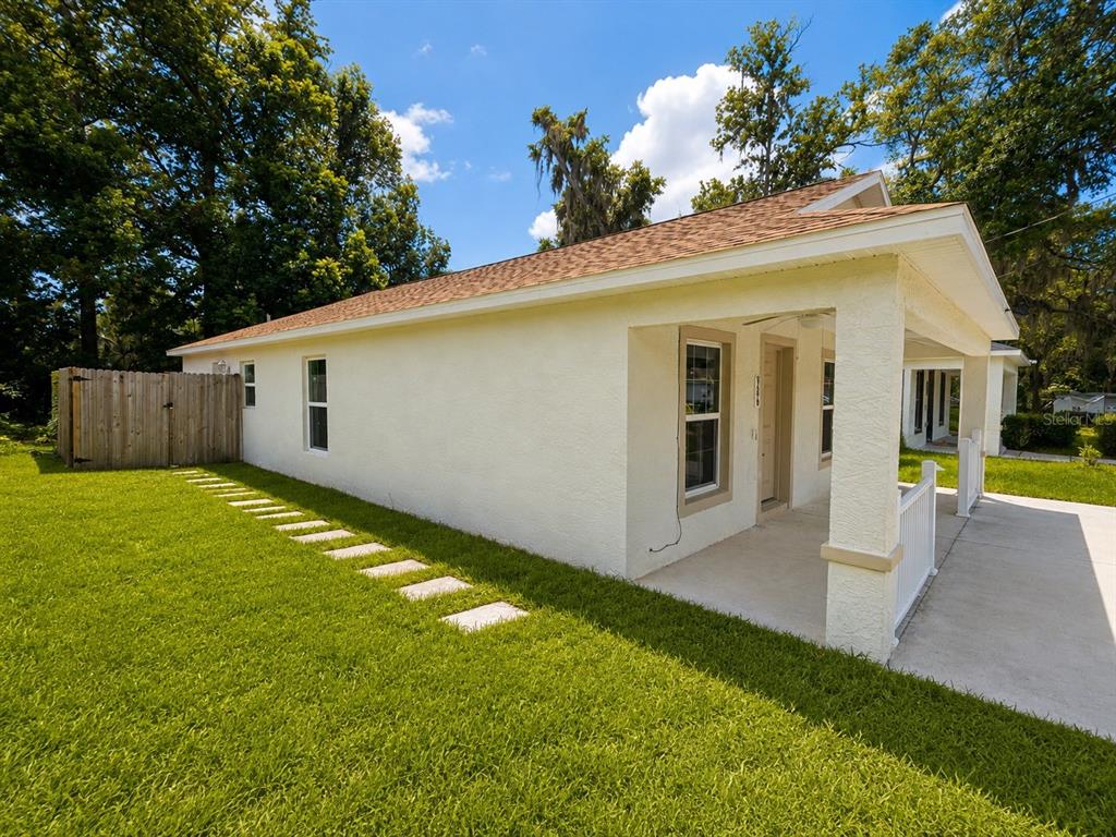 A side view of a light-colored house with a covered porch and a wooden fence — 986 NW 1ST STREET, OCALA, FL