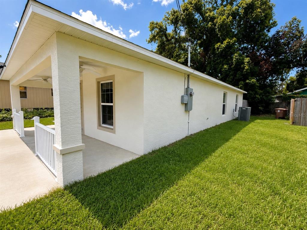 A side view of a white stucco house with a covered porch and a grassy yard — 986 NW 1ST STREET, OCALA, FL