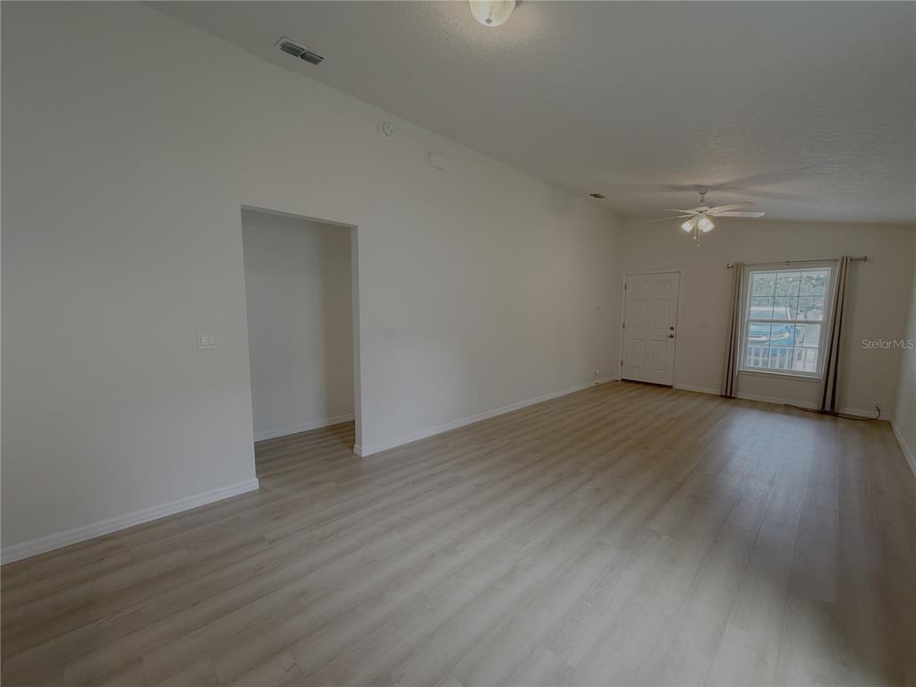 An empty room features light-colored wood-look flooring, white walls, a ceiling fan, and a window — 986 NW 1ST STREET, OCALA, FL