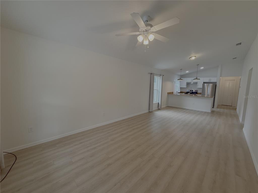 An open-concept living room with light wood-look flooring leads to a kitchen with white cabinets — 986 NW 1ST STREET, OCALA, FL