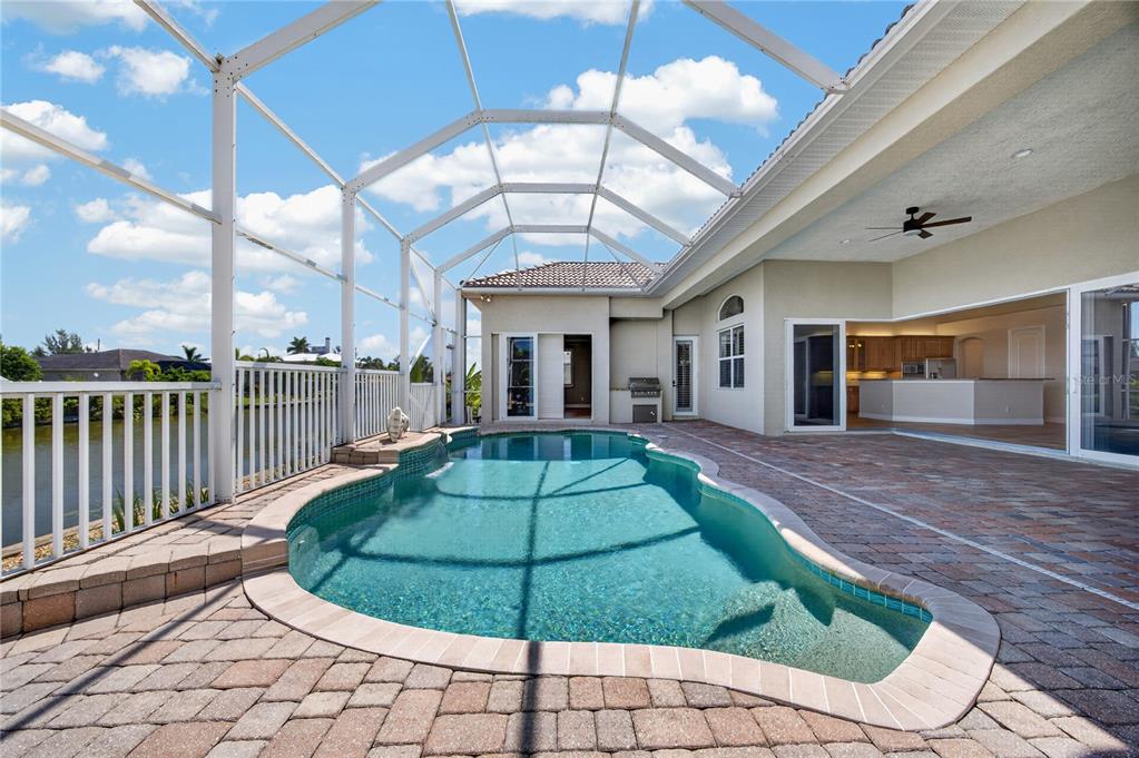 A swimming pool with a screened enclosure sits on a paved patio beside a house — 15140 ALSASK CIRCLE, PORT CHARLOTTE, FL