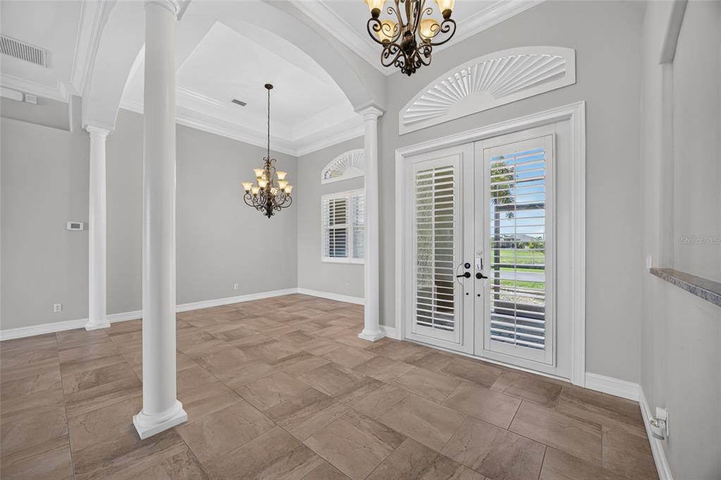 A dining room with tile floors, two chandeliers, white columns, and glass double doors — 15140 ALSASK CIRCLE, PORT CHARLOTTE, FL