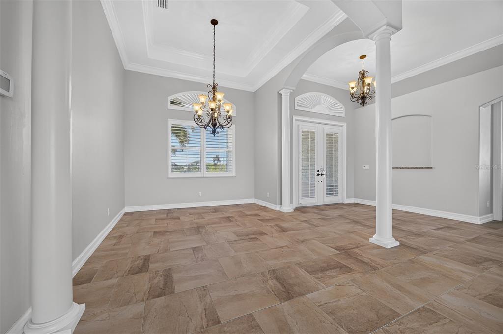 An empty room with light gray walls, tile flooring, two chandeliers, and white columns — 15140 ALSASK CIRCLE, PORT CHARLOTTE, FL