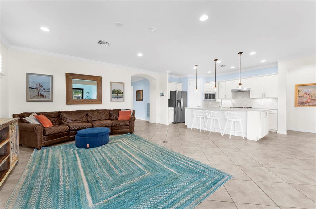 An open-concept living room and kitchen featuring a brown leather sofa and tile flooring — 13908 KARINA STREET, VENICE, FL