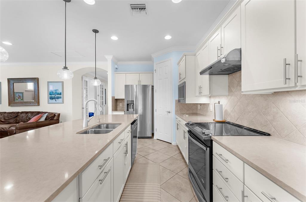 A kitchen features white cabinets, stainless steel appliances, a large island, and light-colored countertops — 13908 KARINA STREET, VENICE, FL