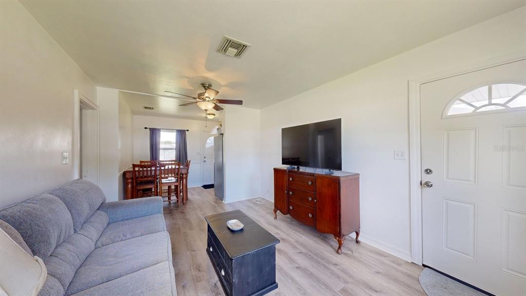 A living room with light wood flooring, a grey sofa, and a wooden media console — 1508 ROSELLE AVENUE, PALATKA, FL