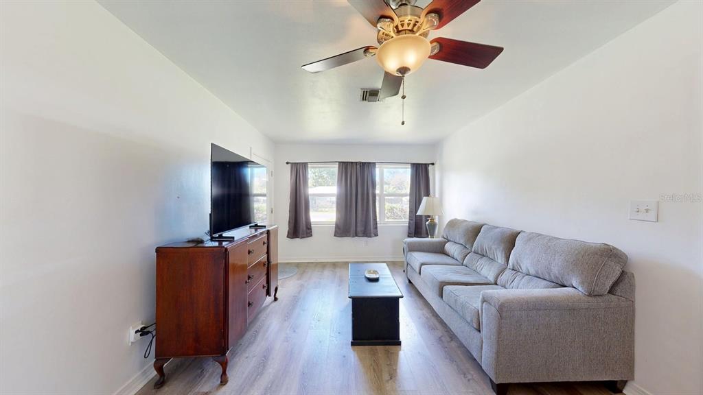 A living room features light wood-look flooring, a gray sofa, a television, and a ceiling fan — 1508 ROSELLE AVENUE, PALATKA, FL