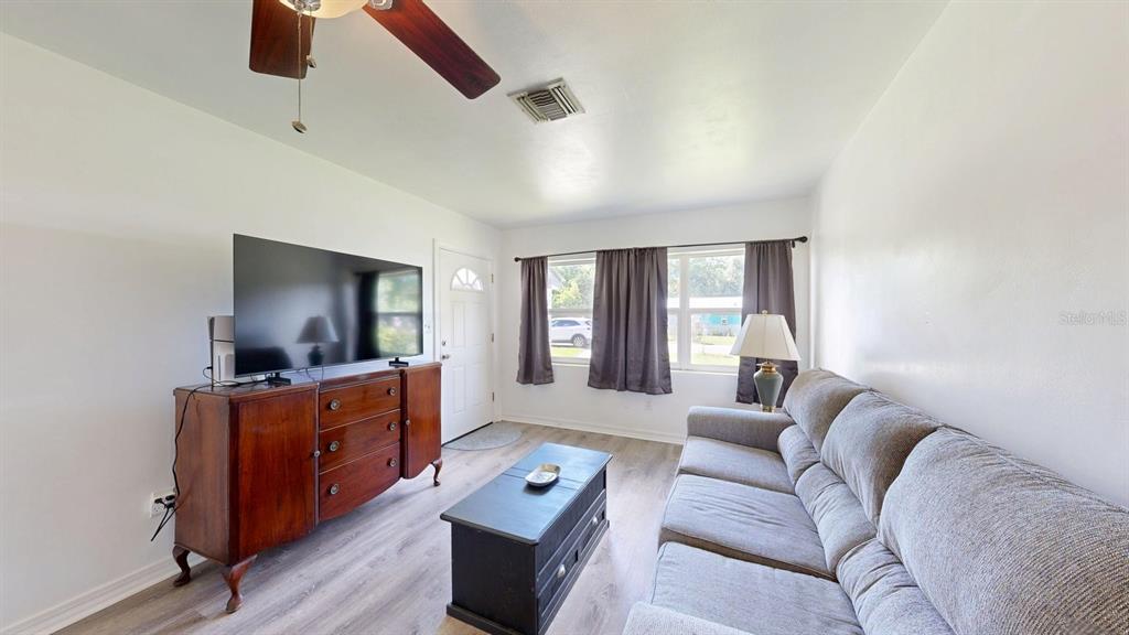 A living room features a grey sofa, a wooden dresser, a coffee table, and windows — 1508 ROSELLE AVENUE, PALATKA, FL