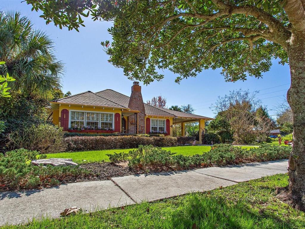 A yellow house with red shutters and a brick chimney sits behind a grassy lawn — 2390 SHERIDAN ROAD, MOUNT DORA, FL