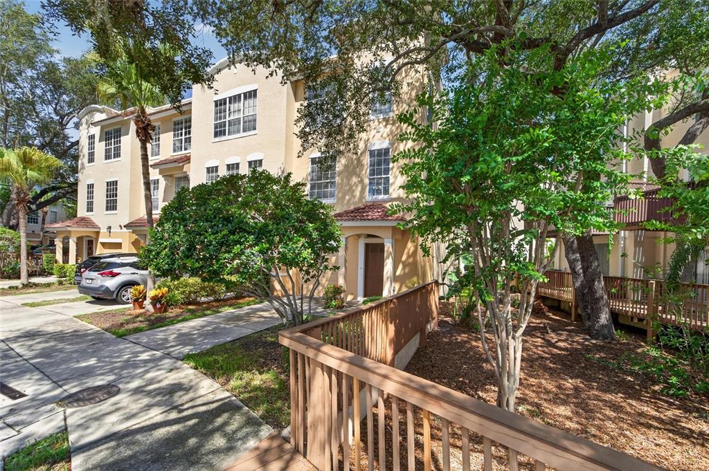 A three-story tan townhouse with a wooden walkway and a car parked in front — 3186 BAYSHORE OAKS DRIVE, TAMPA, FL