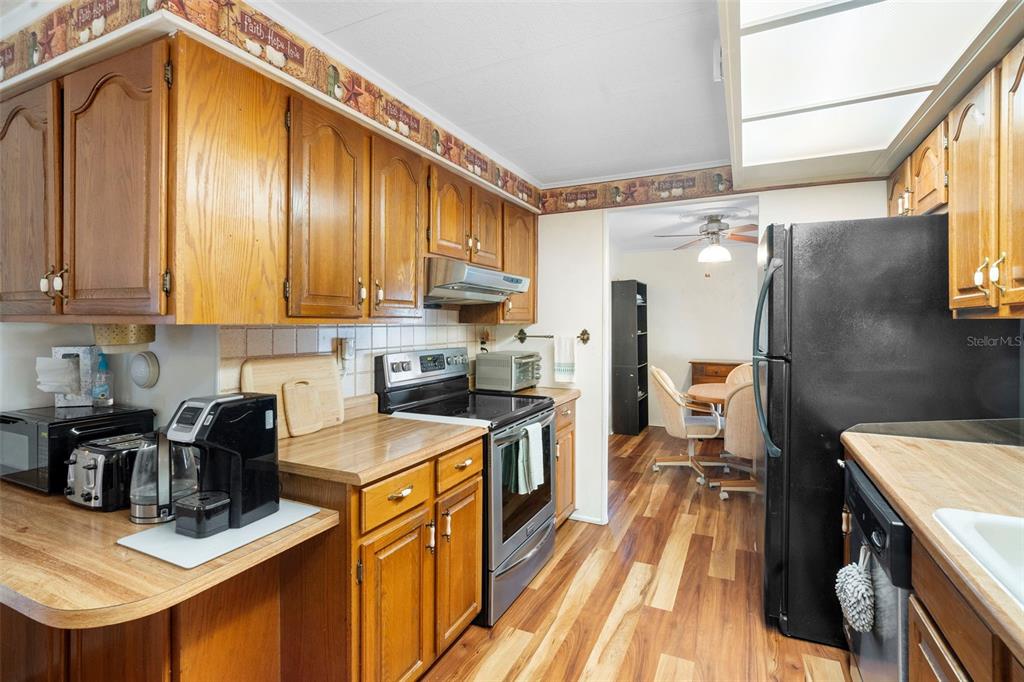 A kitchen with wood cabinets, a black refrigerator, a stainless dishwasher, and a dining area — 232 MEADOW LARK DRIVE, OSTEEN, FL