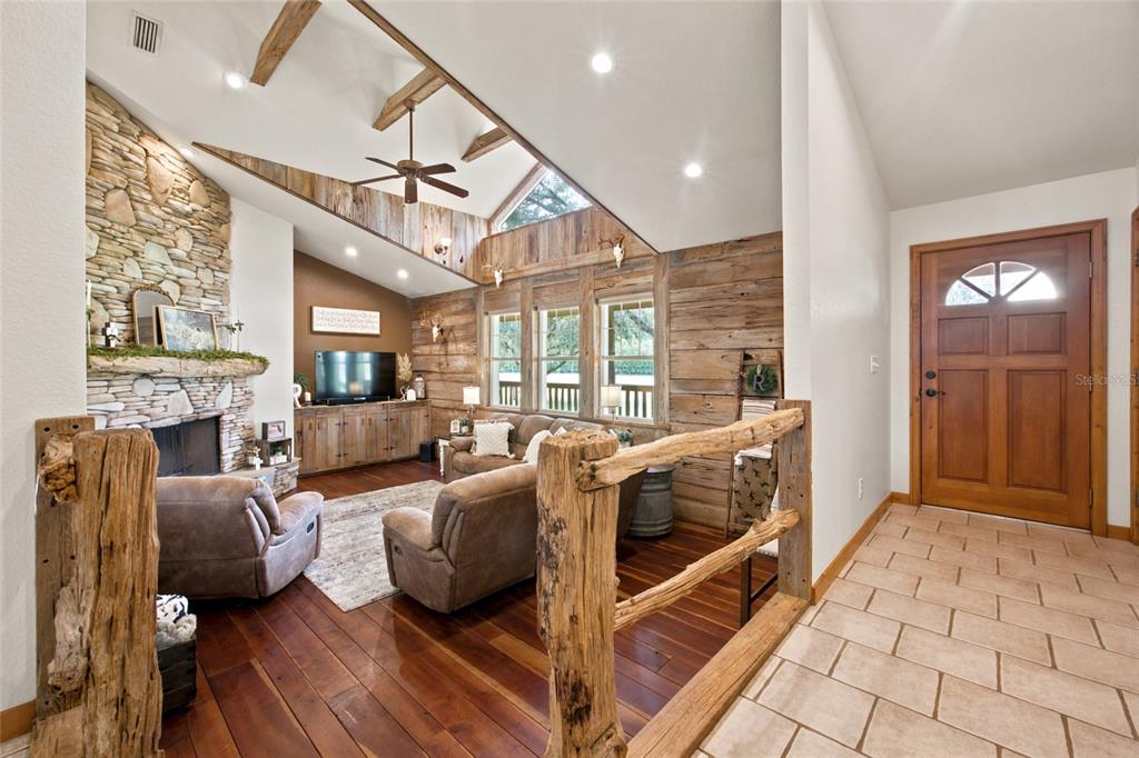 A rustic living room features a stone fireplace, wood-paneled walls, and a vaulted ceiling — 2015 NW 35TH STREET, OCALA, FL