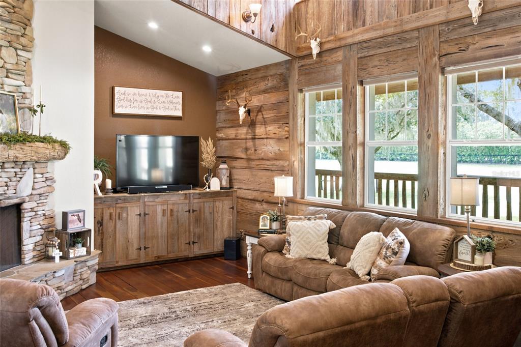 A rustic living room features log walls, a stone fireplace, and brown leather furniture — 2015 NW 35TH STREET, OCALA, FL