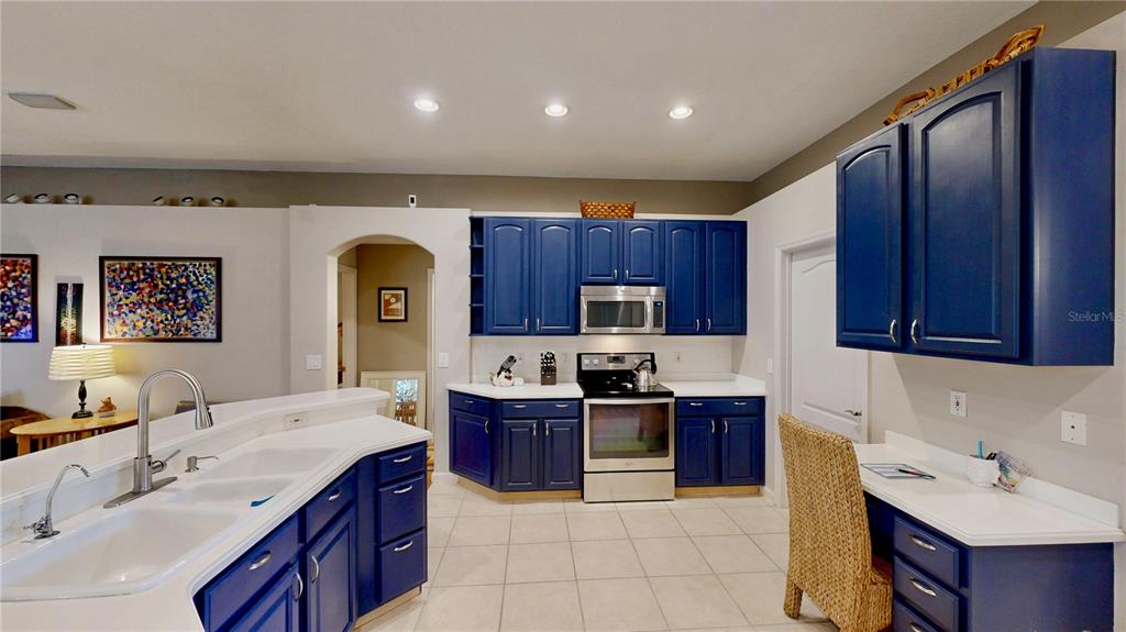 A kitchen features blue cabinets, stainless steel appliances, a white countertop, and a built-in desk — 9101 WOODBRIDGE OAK TERRACE, ORLANDO, FL