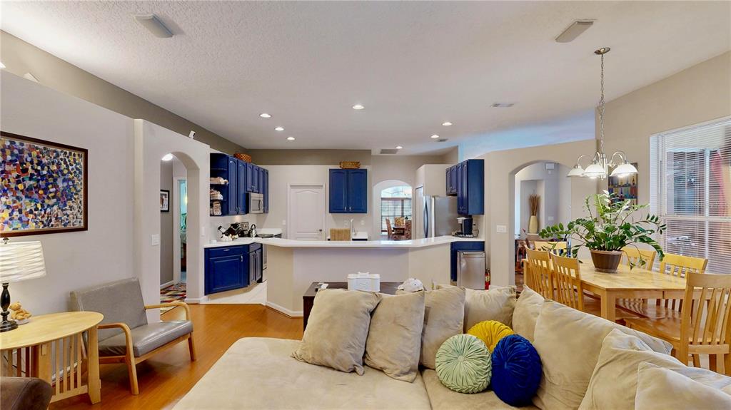 An open-concept living room and kitchen feature blue cabinets, light wood floors, and neutral furniture — 9101 WOODBRIDGE OAK TERRACE, ORLANDO, FL