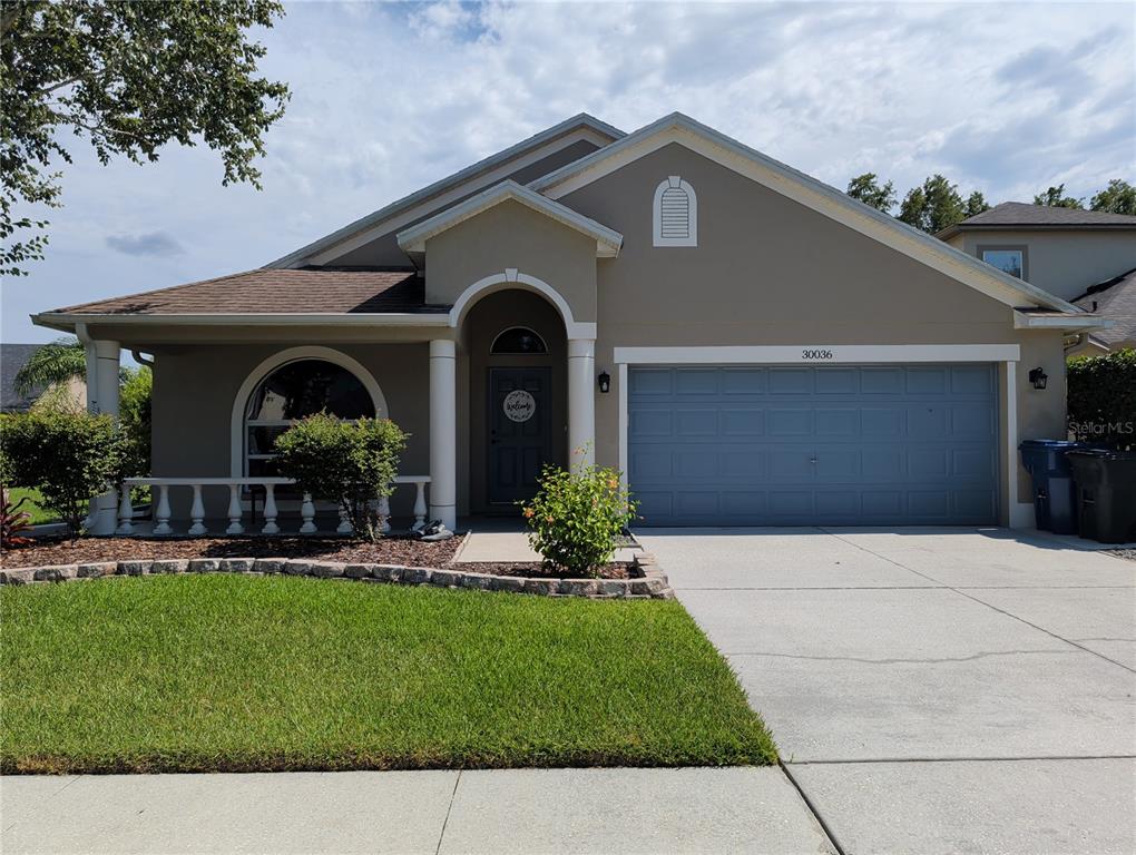 A single-story house with a beige stucco exterior, a two-car garage, and a front porch — 30036 BERMUDA DUNES WAY, WESLEY CHAPEL, FL