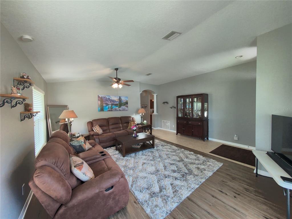 A living room features brown reclining sofas, a patterned area rug, and a dark wood hutch — 30036 BERMUDA DUNES WAY, WESLEY CHAPEL, FL