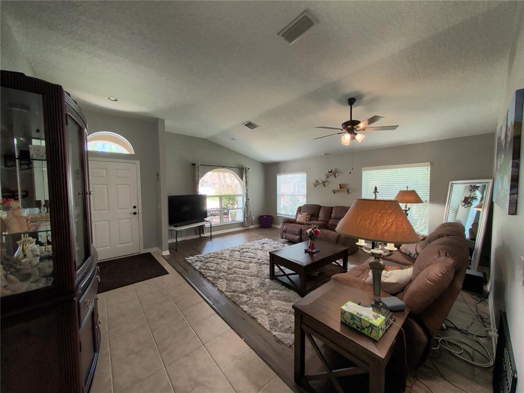 A living room with tile and wood flooring, a vaulted ceiling, and brown leather furniture — 30036 BERMUDA DUNES WAY, WESLEY CHAPEL, FL