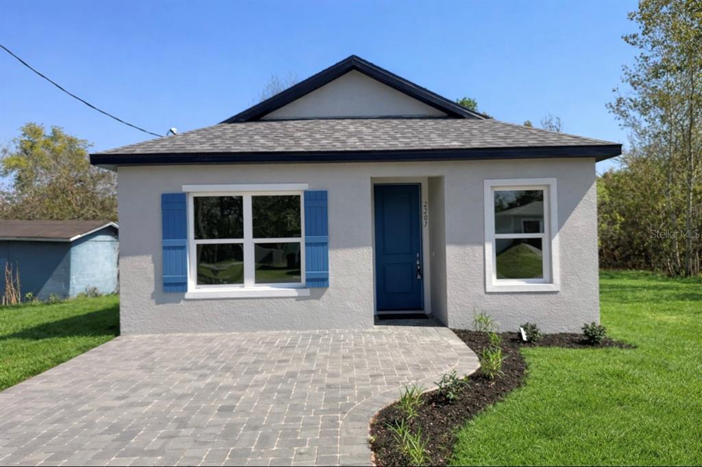 A small, single-story house with gray stucco siding, a blue door, and a paved driveway — 939 MOTON AVENUE, SANFORD, FL
