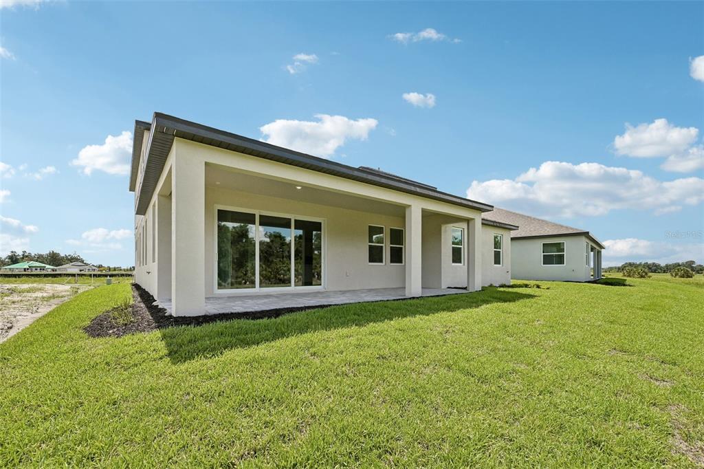 The exterior of a modern house features a covered patio, sliding glass doors, and lawn — 3693 142ND TERRACE E, PARRISH, FL