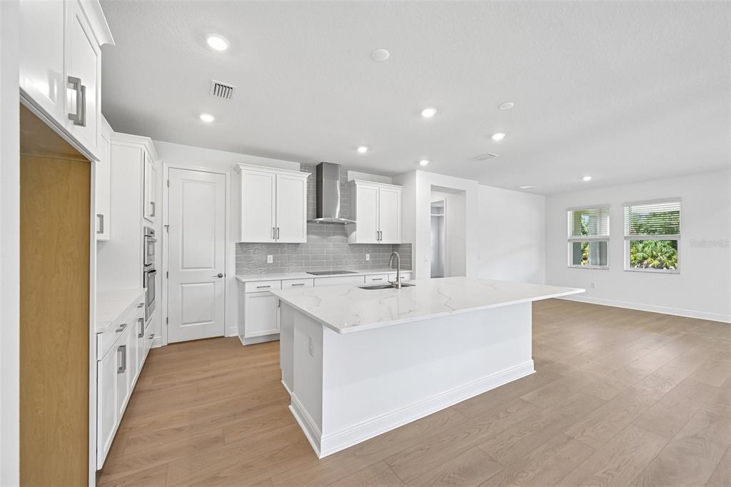 A modern kitchen features white cabinets, a large marble-topped island, and light wood flooring — 3693 142ND TERRACE E, PARRISH, FL