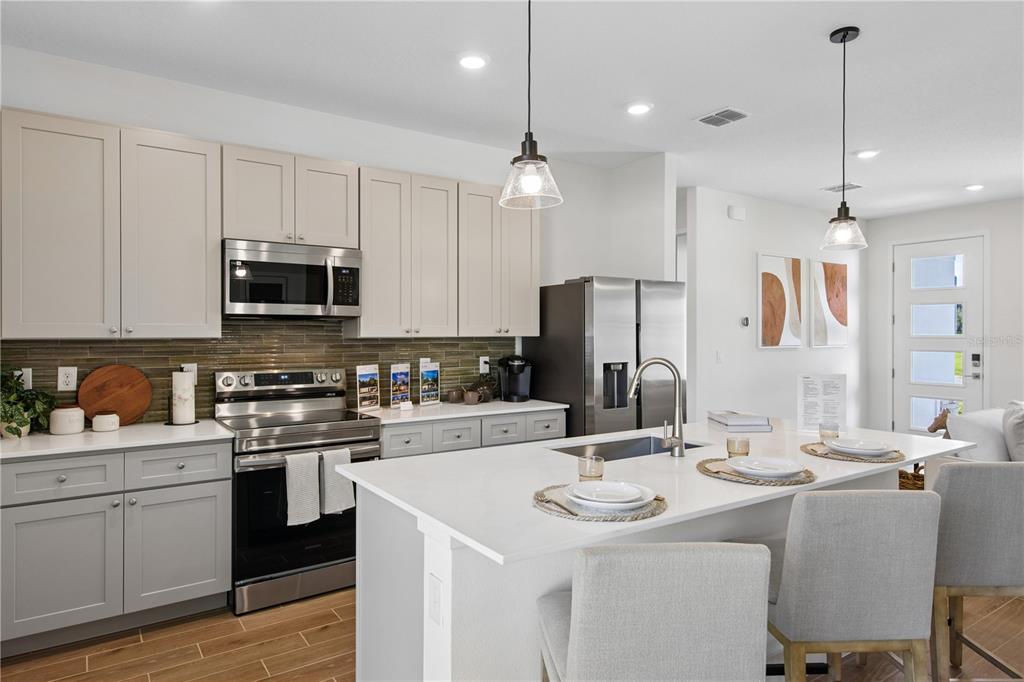 A modern kitchen features light gray cabinets, stainless steel appliances, and a white quartz island — 17 BONNIE LANE, PALM COAST, FL