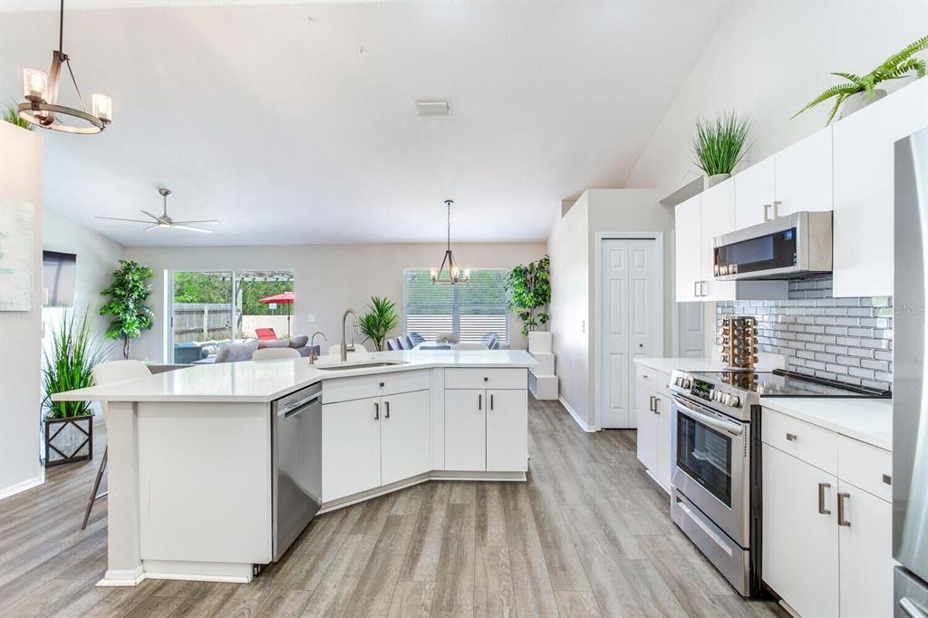 A modern kitchen with white cabinets, stainless steel appliances, and an island overlooks a living area — 1126 VINETREE DRIVE, BRANDON, FL