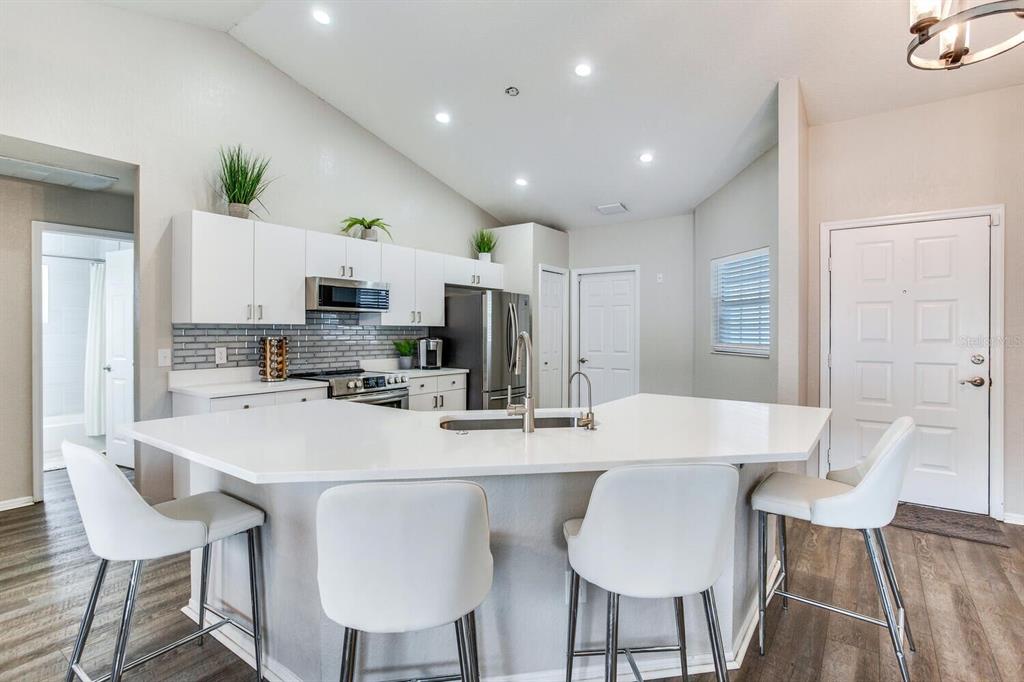 A modern kitchen features white cabinets, a large quartz island with seating, and stainless appliances — 1126 VINETREE DRIVE, BRANDON, FL