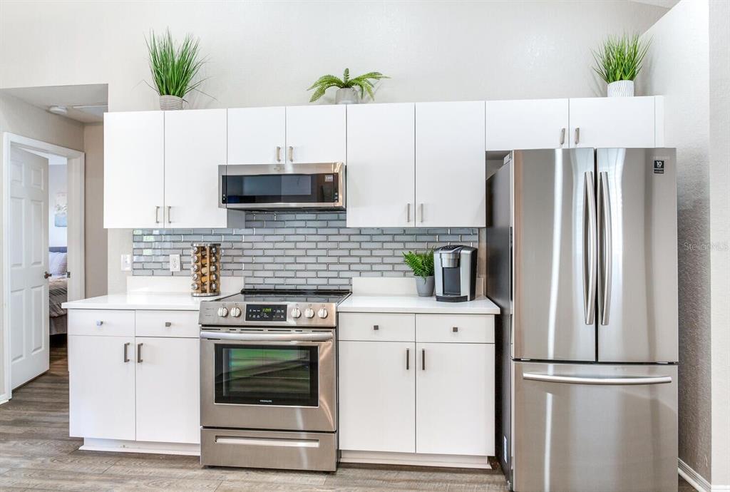 A kitchen features white cabinets, stainless steel appliances, and a gray subway tile backsplash — 1126 VINETREE DRIVE, BRANDON, FL