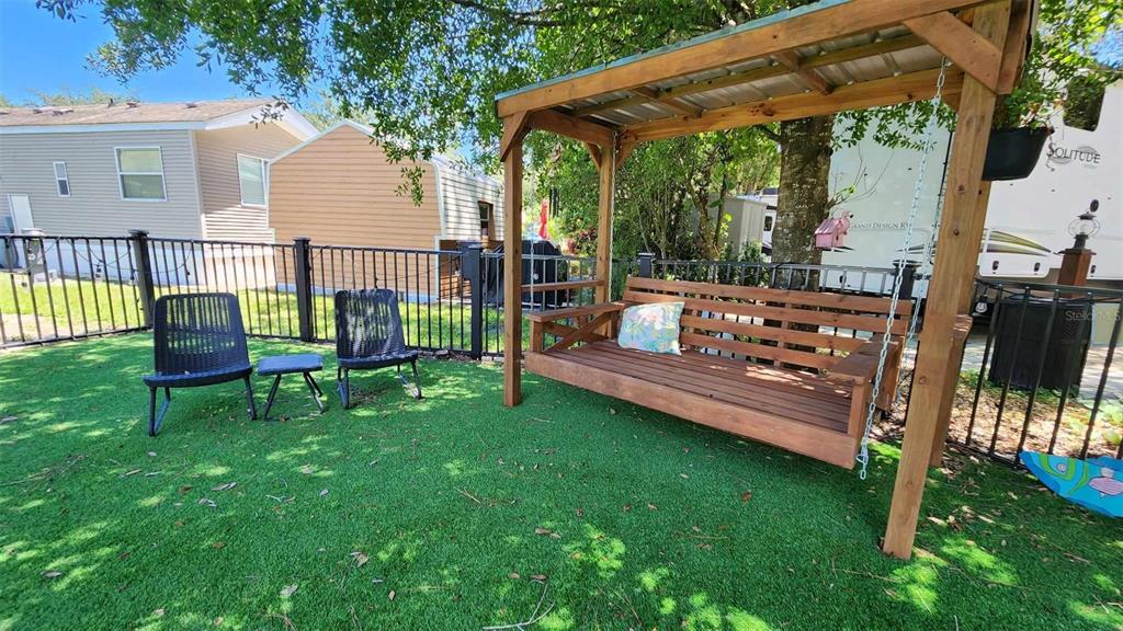A wooden porch swing sits on a patch of artificial turf in a fenced backyard — 53 PALOMINO PATH, RIVER RANCH, FL