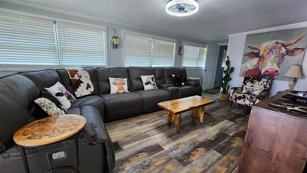 A living room features a large gray sectional sofa, wood-look flooring, and cow-themed decor — 53 PALOMINO PATH, RIVER RANCH, FL