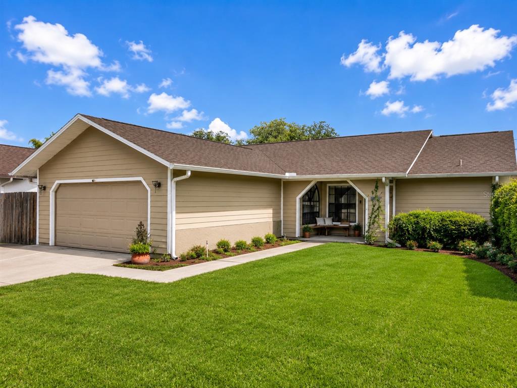 A single-story house with tan siding, a two-car garage, and a green front lawn — 10135 CHESHAM DRIVE, ORLANDO, FL