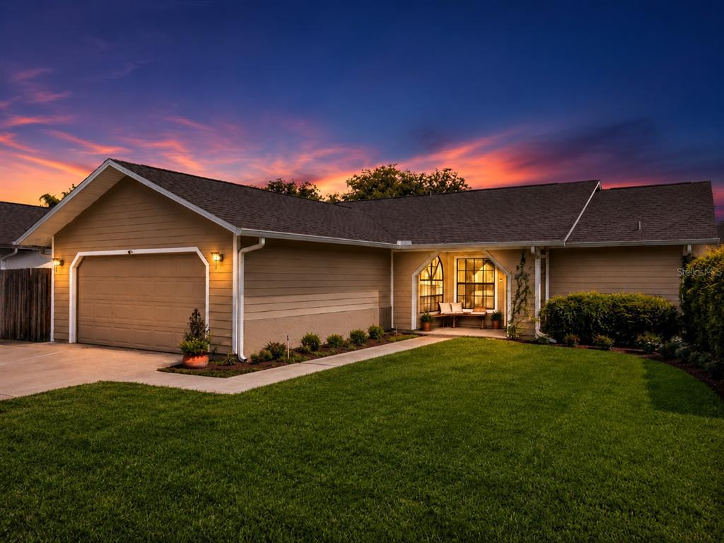 A single-story house with a tan exterior, a two-car garage, and a front lawn at sunset — 10135 CHESHAM DRIVE, ORLANDO, FL