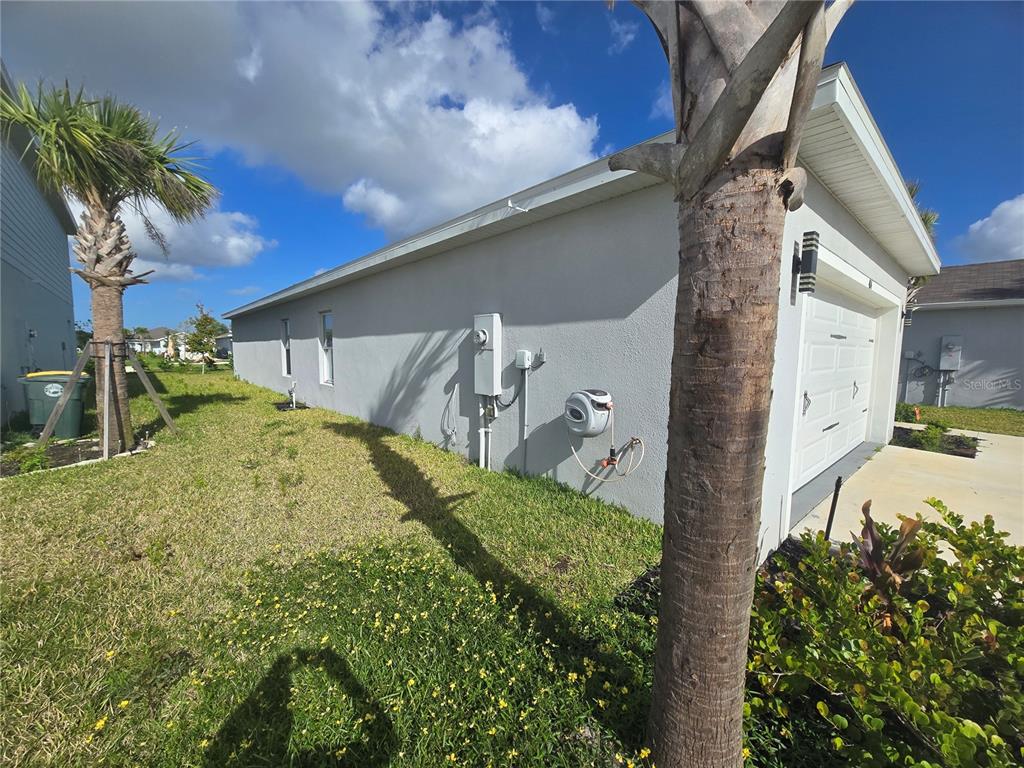 The exterior side of a house features a gray stucco wall, a garage, and landscaping — 404 ACAI LANE, FORT PIERCE, FL