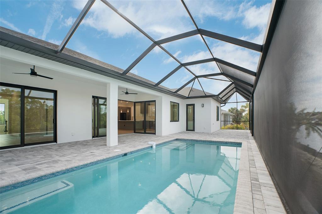 A swimming pool sits on a paved patio enclosed by a large screened-in lanai — 13192 WINDCREST DRIVE, PORT CHARLOTTE, FL