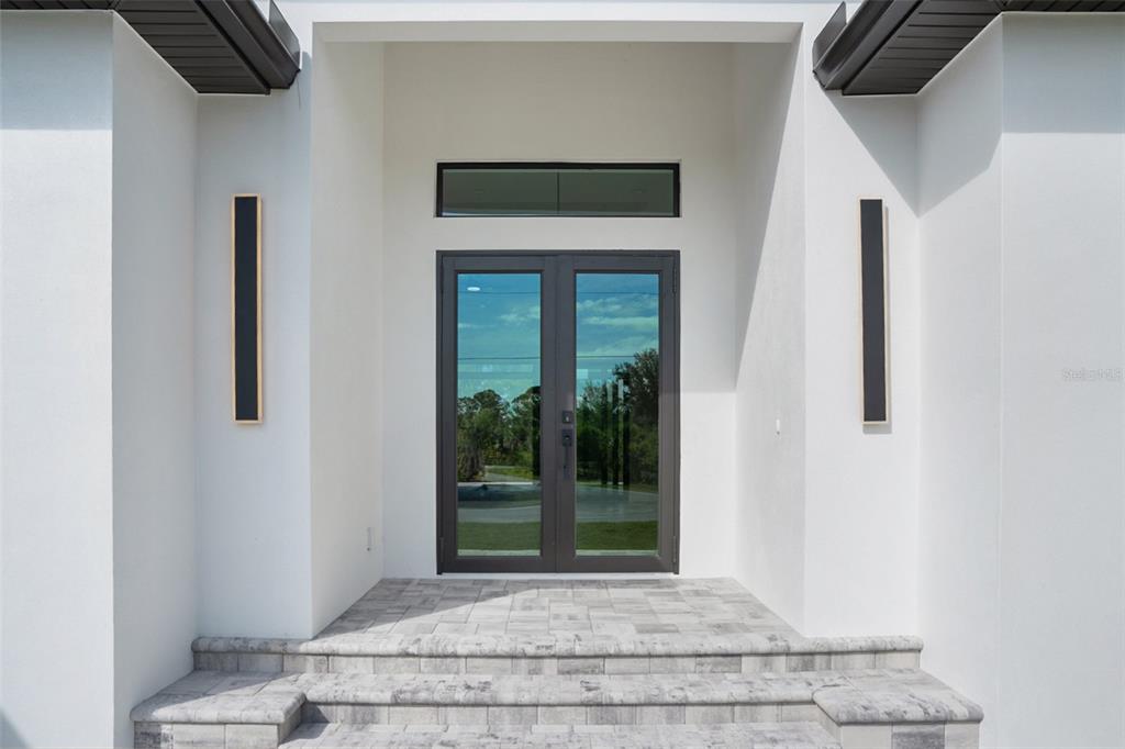 A modern entryway features double glass doors, a transom window, and two vertical wall sconces — 13192 WINDCREST DRIVE, PORT CHARLOTTE, FL