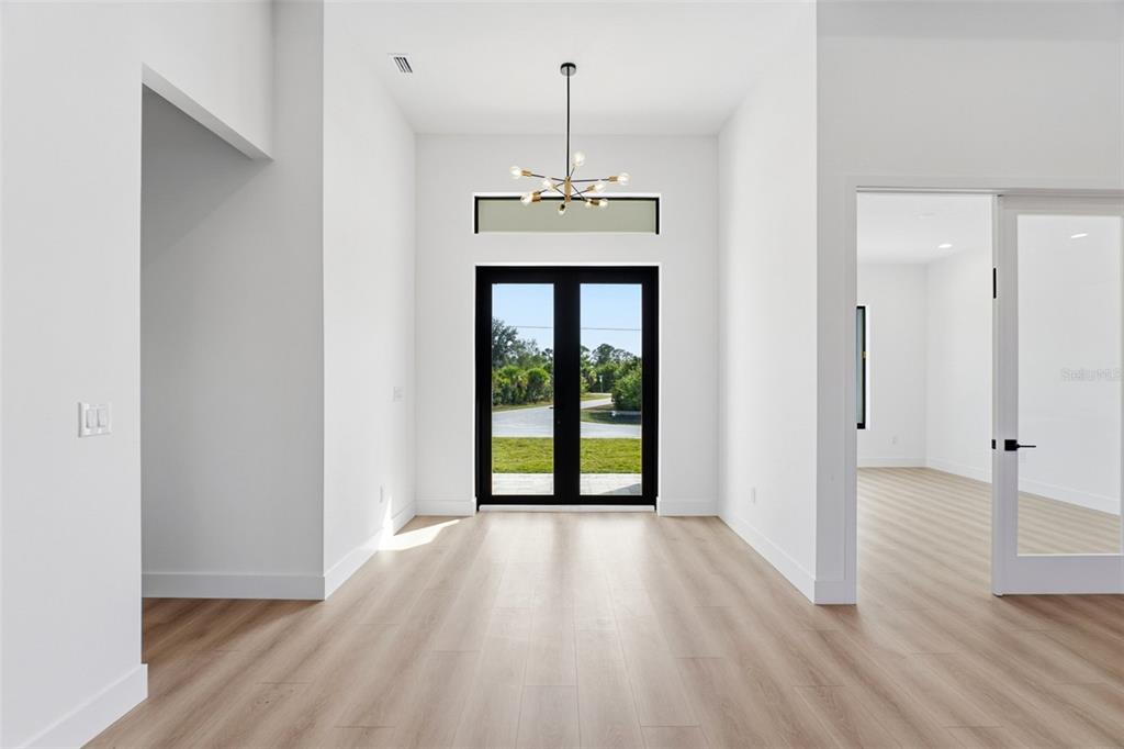 A bright entryway features light wood flooring, white walls, a modern chandelier, and black-framed doors — 13192 WINDCREST DRIVE, PORT CHARLOTTE, FL