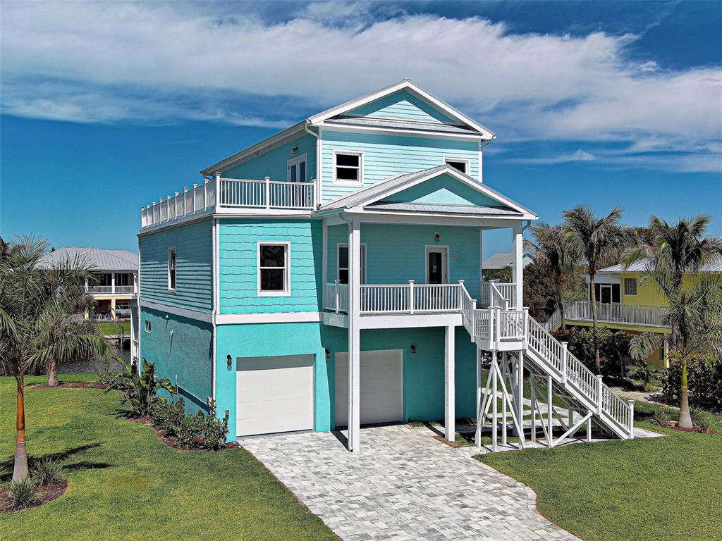 A three-story, light blue coastal home features a garage, elevated porch, and outdoor staircase — 13095 VIA CASSIA, PLACIDA, FL