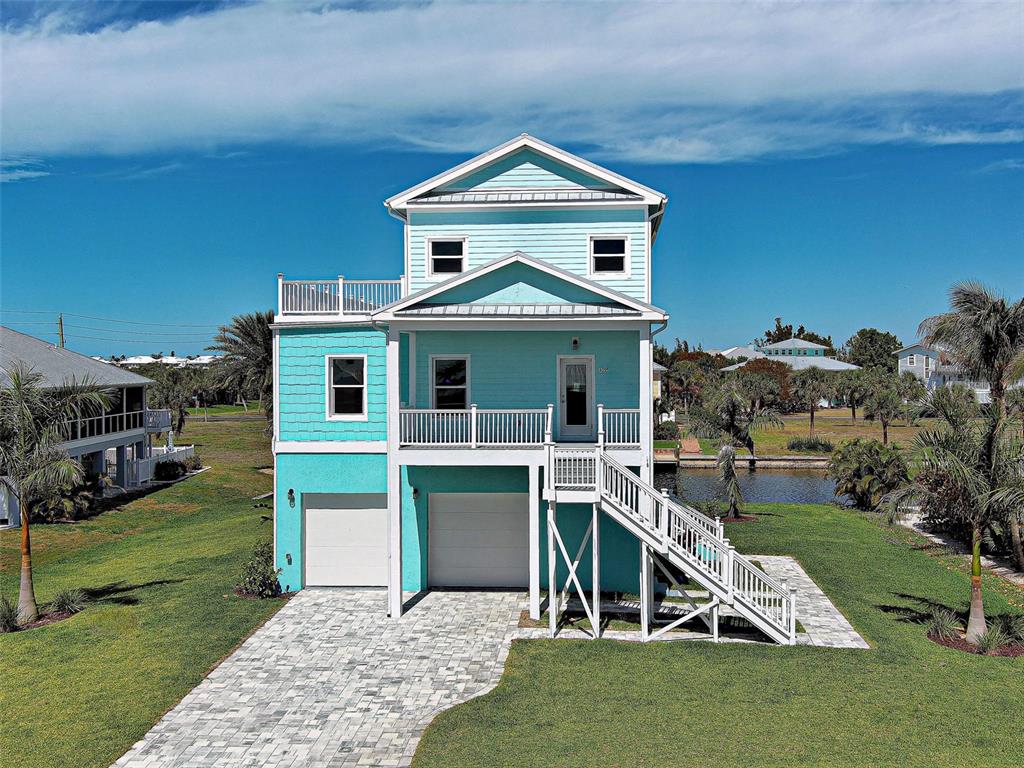 A three-story, light blue coastal home with a paved driveway and an elevated front porch — 13095 VIA CASSIA, PLACIDA, FL