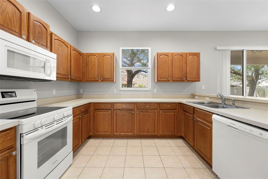 A kitchen features oak cabinets, white appliances, beige countertops, and light-colored tile flooring — 10215 CYPRESS KNEE CIRCLE, ORLANDO, FL