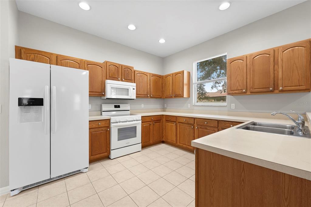 A kitchen features light-colored countertops, wood cabinets, white appliances, and tiled flooring — 10215 CYPRESS KNEE CIRCLE, ORLANDO, FL