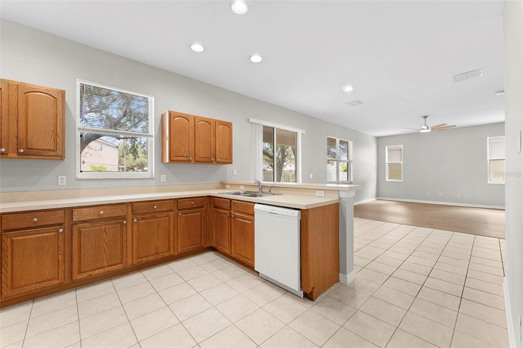 A kitchen with wood cabinets, beige countertops, and tile flooring opens to a living area — 10215 CYPRESS KNEE CIRCLE, ORLANDO, FL